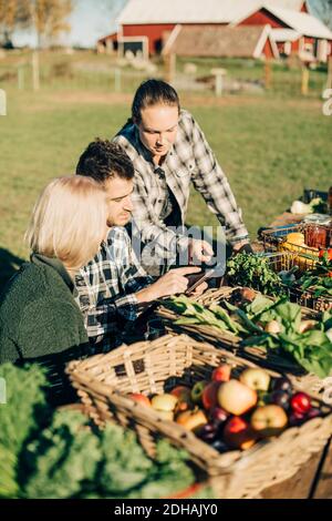 Agriculteurs masculins et féminins utilisant des tablettes numériques avec des légumes biologiques sur la table Banque D'Images