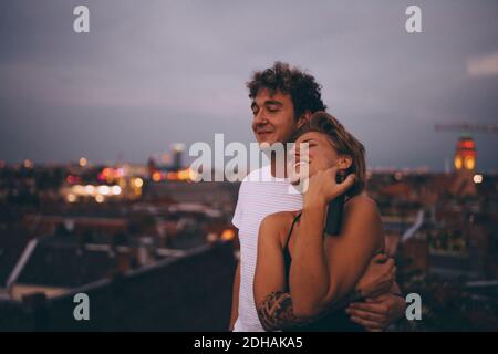 Couple aimant embrassant en se tenant sur la terrasse contre le ciel à crépuscule Banque D'Images