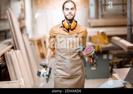 Portrait d'un beau charpentier en uniforme avec des outils modernes à l'atelier de menuiserie Banque D'Images