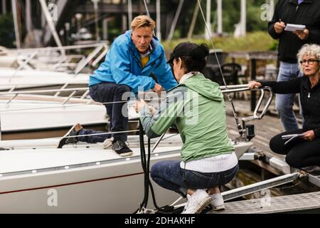 Homme et femme senior regardant une femme instructeur nouant la corde sur la rampe de yacht pendant le cours de maître de bateau Banque D'Images