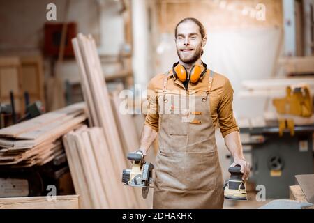 Portrait d'un beau charpentier en uniforme avec des outils modernes à l'atelier de menuiserie Banque D'Images