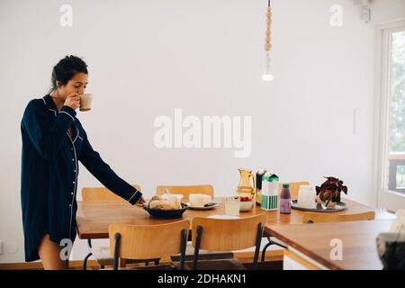 Femme buvant du café tout en regardant le petit déjeuner à table mur Banque D'Images
