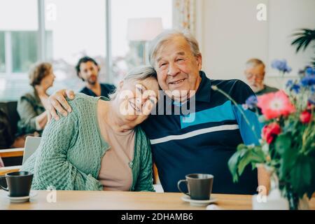 Portrait d'amis âgés assis avec le bras autour à table de salle à manger dans la maison de soins infirmiers Banque D'Images