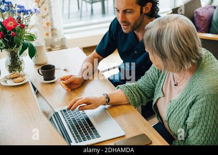 Soignant homme confiant aidant une femme senior à faire des achats en ligne avec carte de crédit et ordinateur portable dans la maison de soins infirmiers Banque D'Images