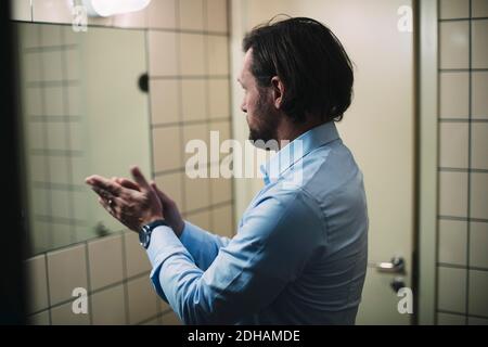 Homme d'affaires se frottant les mains en se tenant devant le miroir salle de bains Banque D'Images