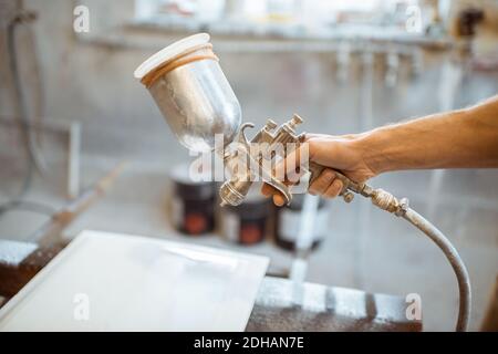 Peindre un produit en bois avec un pistolet à peinture à l'atelier de peinture de la charpenterie, gros plan Banque D'Images