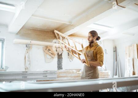 Beau menuisier vérifiant la qualité du cadre de la fenêtre avant la peinture à l'atelier de menuiserie Banque D'Images