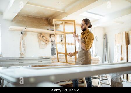 Beau menuisier vérifiant la qualité du cadre de la fenêtre avant la peinture à l'atelier de menuiserie Banque D'Images