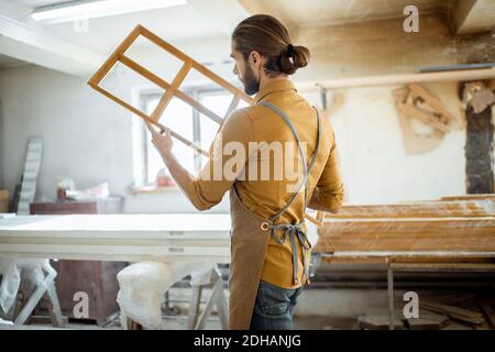 Beau menuisier vérifiant la qualité du cadre de la fenêtre avant la peinture à l'atelier de menuiserie Banque D'Images