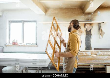 Beau menuisier vérifiant la qualité du cadre de la fenêtre avant la peinture à l'atelier de menuiserie Banque D'Images