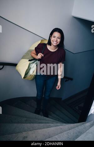 Portrait en grand angle d'une femme souriante portant un sac debout sur les marches Banque D'Images