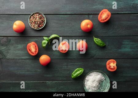 Une photo en hauteur de tomates biologiques et de basilic frais feuilles sur fond rustique foncé avec sel et poivre Banque D'Images