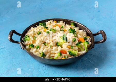 Riz vegan sauté au brocoli, pois doux et carrotes, dans une casserole sur fond bleu Banque D'Images