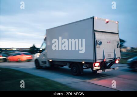 Le camion de livraison se déplace sur la route dans la ville contre le ciel à coucher de soleil Banque D'Images