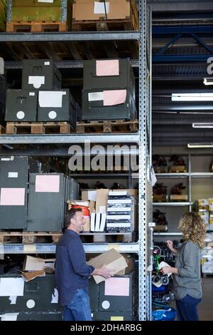 Vue latérale d'un homme mûr souriant et volontaire debout avec une femme collègue par rack à l'entrepôt Banque D'Images