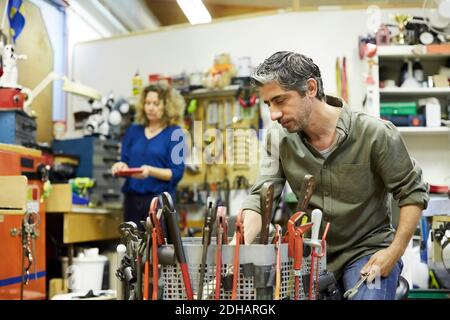 Un homme mature travaillant avec des outils contre une collègue féminine chez atelier Banque D'Images