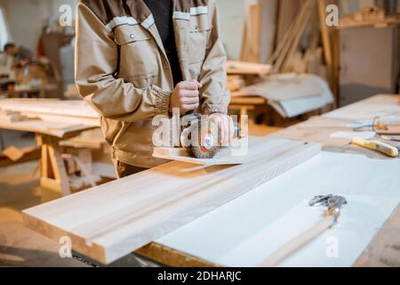 Beau menuisier dans le bois de brossage uniforme avec machine à main à la fabrication de menuiserie Banque D'Images