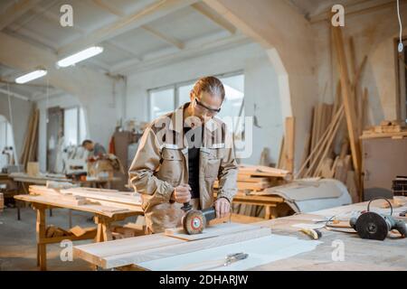 Beau menuisier dans le bois de brossage uniforme avec machine à main à la fabrication de menuiserie Banque D'Images