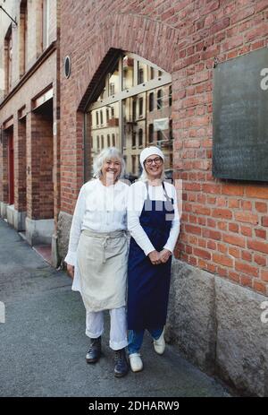 Portrait de boulangers féminins souriants debout près du mur de briques à l'extérieur boulangerie Banque D'Images
