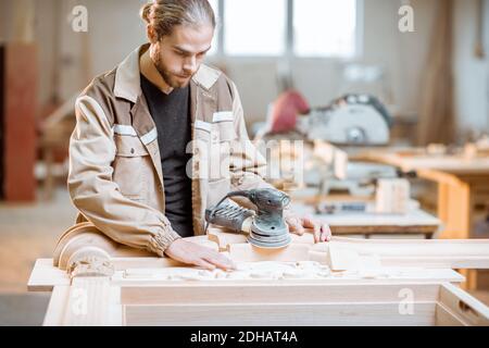 Beau menuisier vérifie la qualité de sculpture d'un produit de menuisier à la fabrication de menuiserie Banque D'Images