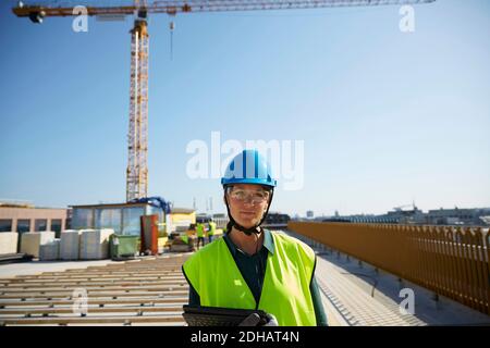 Femme ingénieure confiante en vêtements réfléchissants avec tablette numérique AT chantier contre ciel dégagé Banque D'Images