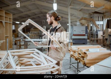 Beau menuisier vérifiant la qualité du cadre de la fenêtre avant la peinture à l'atelier de menuiserie Banque D'Images