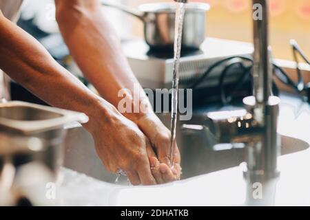 Image rognée du chef masculin se lavant les mains dans l'évier à cuisine commerciale Banque D'Images