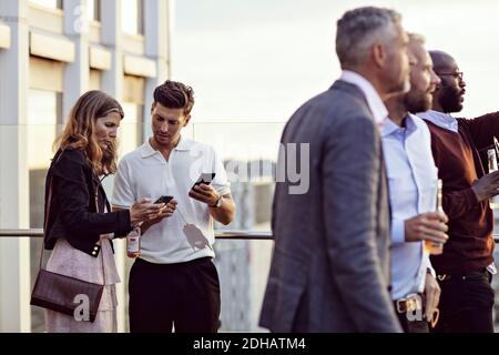 Professionnels parlant sur smartphone pendant que leurs collègues apprécient leur bureau fête après le travail Banque D'Images