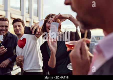 Vos collègues professionnels prennent des souvenirs tout en photographiant avec des smartphones à fêtes après le travail sur la terrasse Banque D'Images