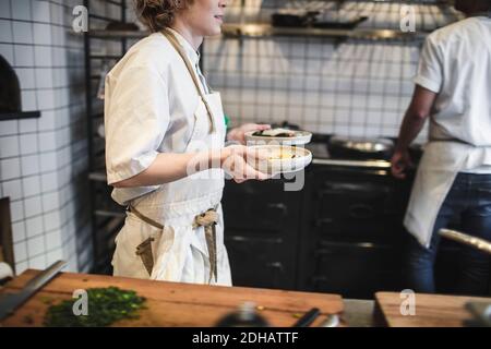 Section intermédiaire de serveuse transportant des assiettes dans la cuisine du restaurant Banque D'Images