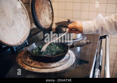 Main de chef cuisiné en remuant le chou kale dans une casserole cuisinière dans la cuisine du restaurant Banque D'Images