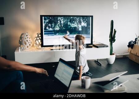 S'agenouiller sur toute la longueur du garçon tout en touchant la Smart TV salle de séjour à la maison Banque D'Images