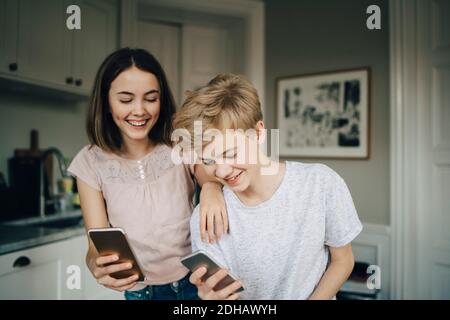 Des amis hommes et femmes heureux tenant des smartphones dans la cuisine à la maison Banque D'Images