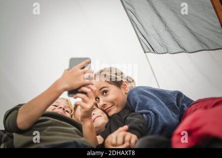 Garçon prenant le selfie avec des sœurs en étant allongé dans une tente Banque D'Images