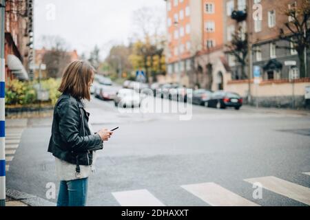 Vue latérale d'une fille à l'aide d'un téléphone portable rue de la ville Banque D'Images