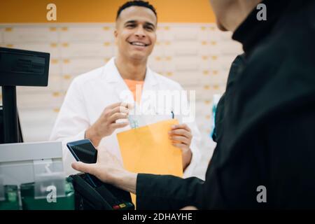 Section intermédiaire d'une cliente senior utilisant le paiement sans contact via SMART téléphonez contre le pharmacien à la caisse dans le bts Banque D'Images