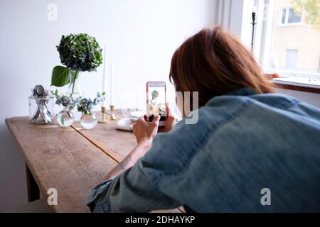 Vue arrière d'un blogueur qui photographie les vases floraux sur la table téléphone portable Banque D'Images