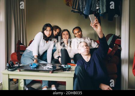 Des amis qui prennent leur selfie sur leur smartphone tout en faisant des visages salle de séjour à la maison Banque D'Images