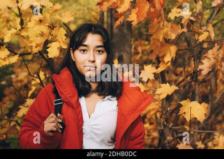 Portrait d'une adolescente confiante portant une veste rouge debout contre érables Banque D'Images