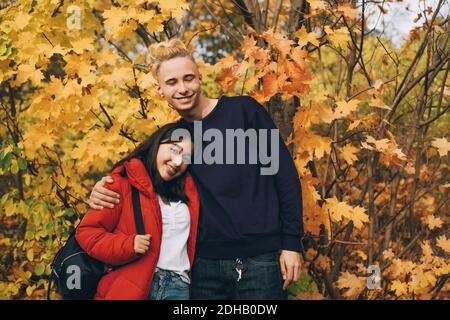 Des amis adolescents souriants se tenant contre des érables à l'automne Banque D'Images