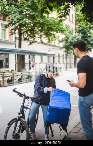Liveuse tenant le sac pendant que le client est debout sur le trottoir en ville Banque D'Images