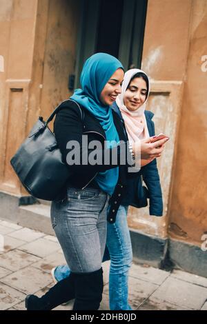 Jeune femme souriante marchant avec une amie tenant un smartphone en ville Banque D'Images