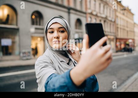 Une jeune femme musulmane confiante prend le selfie dans la rue de la ville Banque D'Images