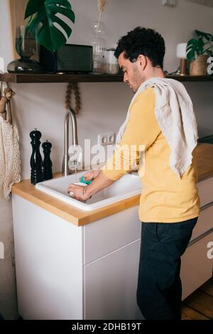 Vue latérale de l'ustensile de lavage homme moyen à l'évier dans la cuisine Banque D'Images