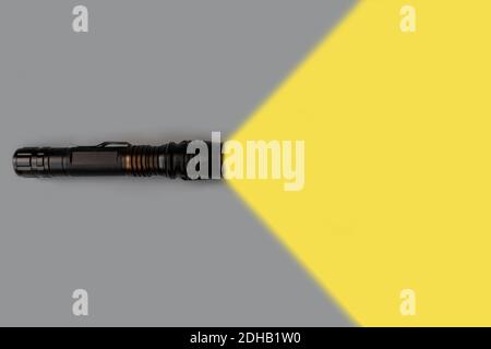 La lampe de poche est allumée avec un faisceau lumineux jaune sur fond gris et un emplacement vide pour le texte. Vue de dessus. Concept créatif minimal. Couleur 2021. Banque D'Images