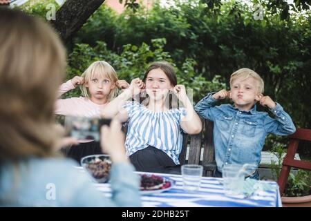 Femme photographiant des enfants tout en faisant des visages à la table de salle à manger fête de jardin Banque D'Images