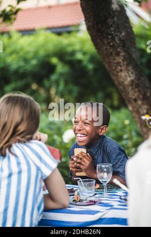 Un garçon joyeux tenant le téléphone tout en étant assis à la table de salle à manger arrière-cour Banque D'Images