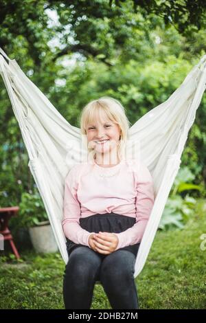 Portrait d'une fille souriante assise sur une balançoire blanche dans l'arrière-cour pendant le week-end Banque D'Images