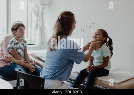 Femme médecin examinant la fille souriante pendant que la famille est assise dans un médecin chambre Banque D'Images