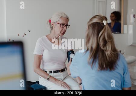 Femme médecin vérifiant la pression artérielle de la femme âgée en clinique Banque D'Images